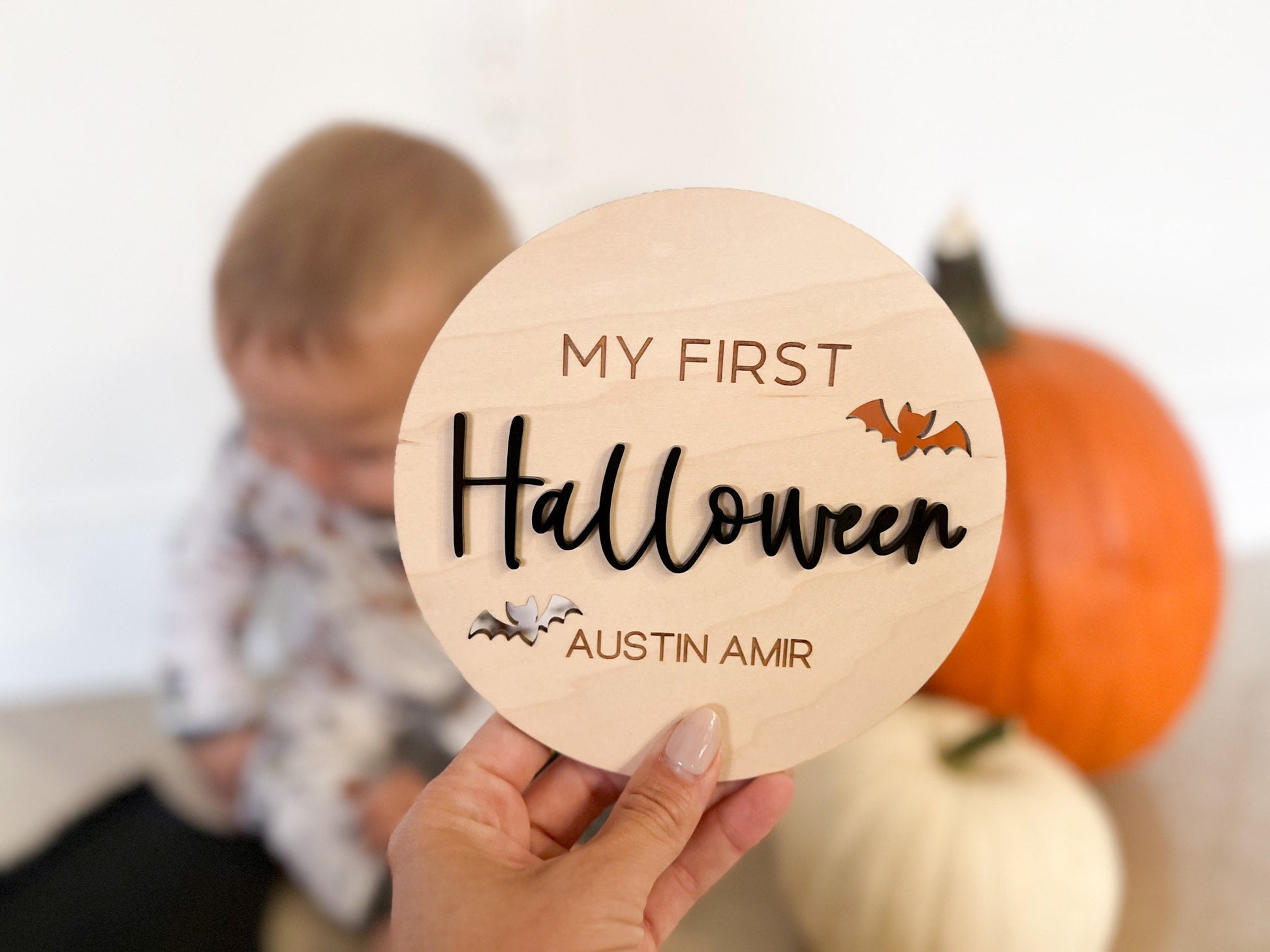 Baby's First Halloween Photo Prop held by hand in front of a baby and a pumpkin, featuring black 3D acrylic lettering