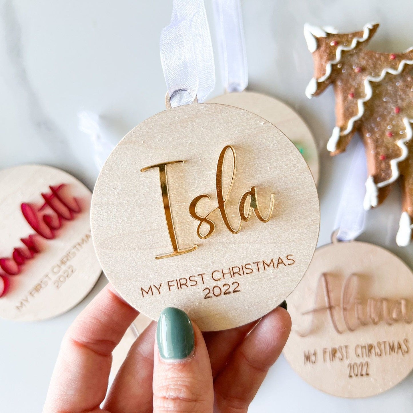 Wooden Milestone Ornament with a shiny gold mirror acrylic name ("Isla") hanging on a flocked Christmas tree.