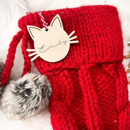 Wooden Cat Head Stocking Tag with "Emily" engraved, shown hanging from a red stocking with fuzzy trim.