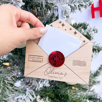 Personalized Wooden Envelope Ornament shown hanging on a green Christmas tree branch with handwritten letter being inserted.