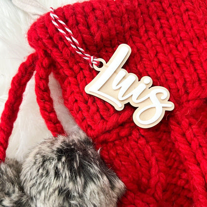 Close-up of 3D Layered Name Christmas Tag ("Luis") with white acrylic on wood, hanging from a red knit stocking.