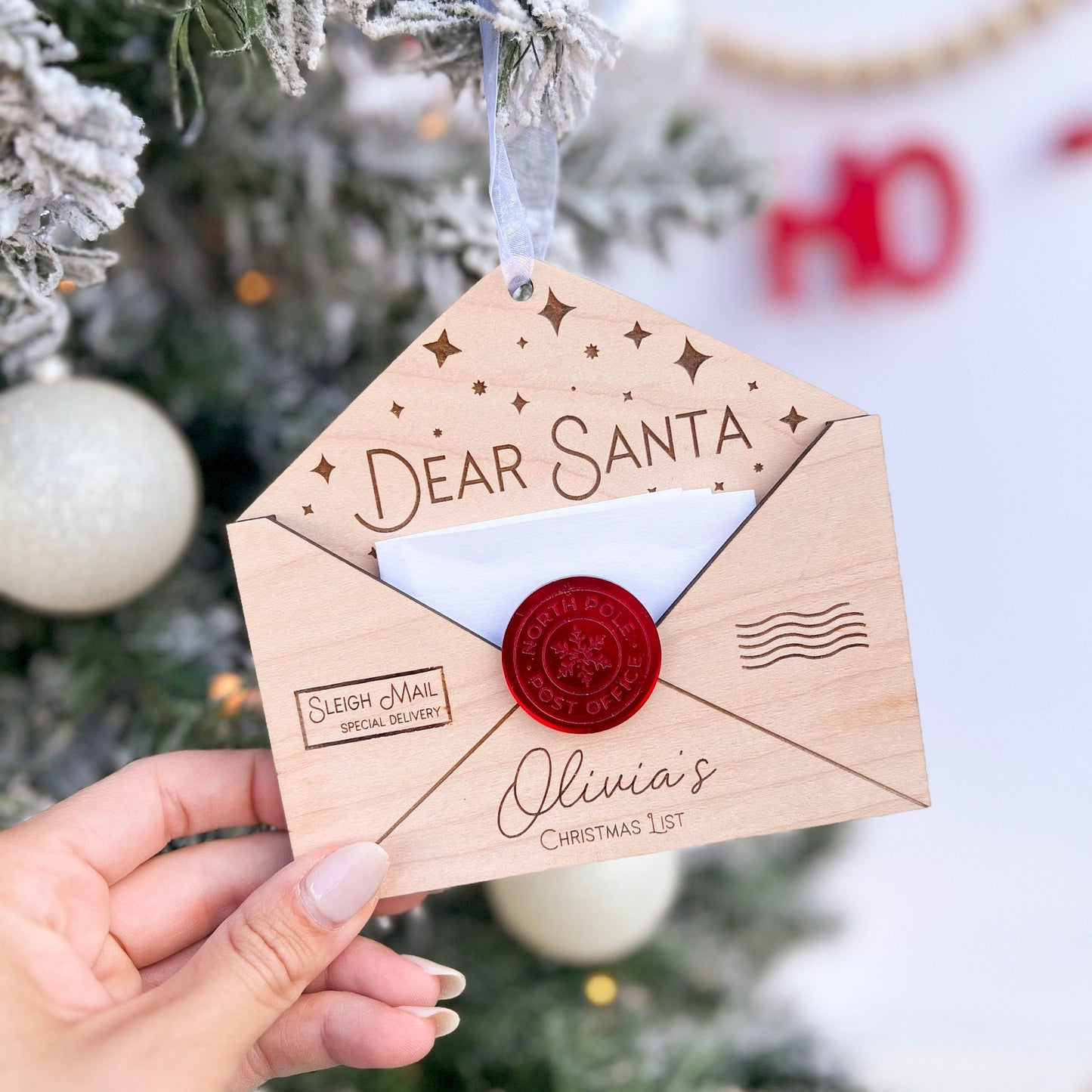 Hand holding the Wooden Christmas Wish List Ornament, showing the texture of the maple plywood and the delicate envelope shape.