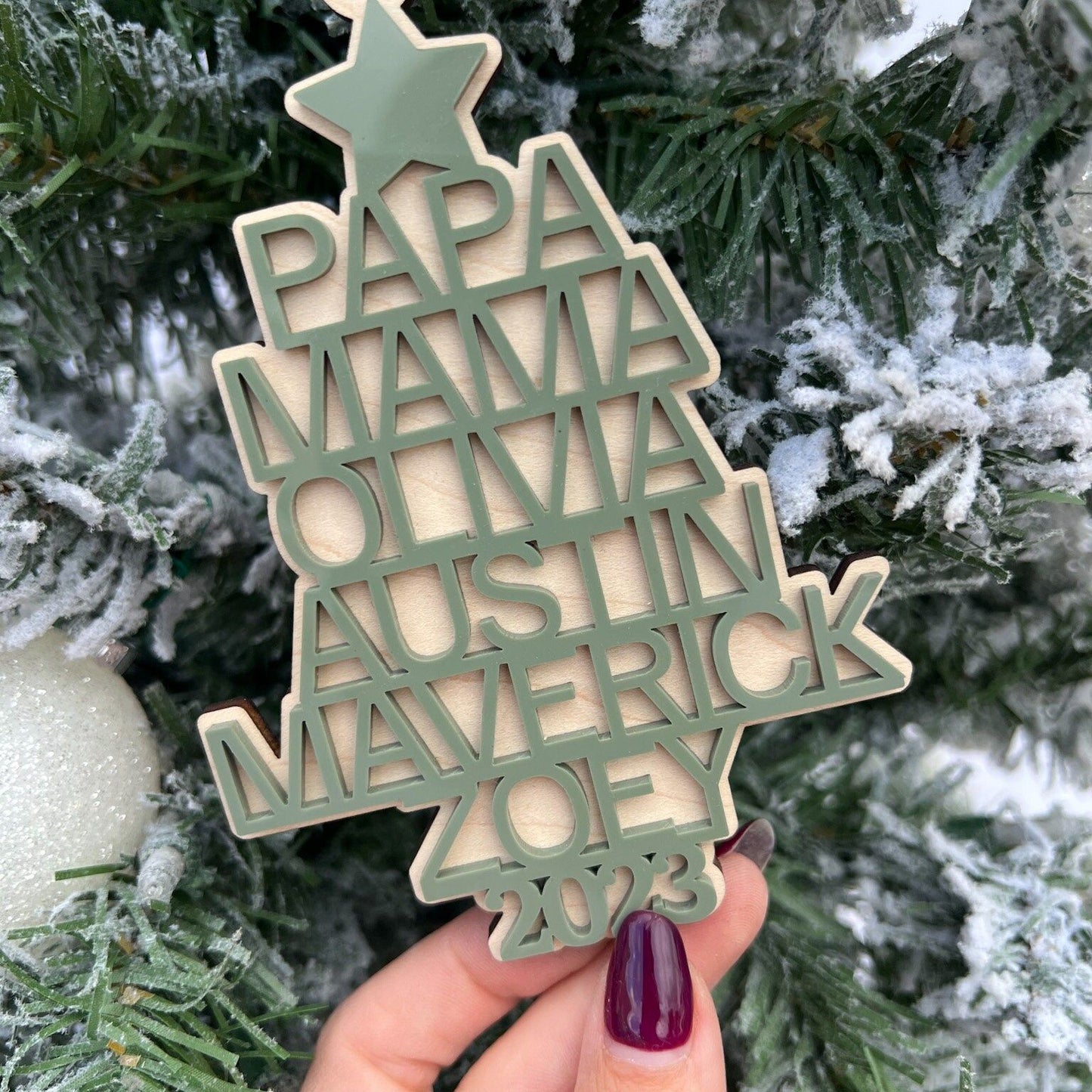 Hand holding the Family Heirloom Ornament, showcasing the thickness of the maple plywood base and the dimensional look of the 3D names.