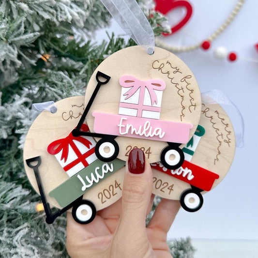 Group of Baby's Christmas Ornaments side-by-side, showcasing different custom wagon and bow color options (e.g., green wagon with a red bow).