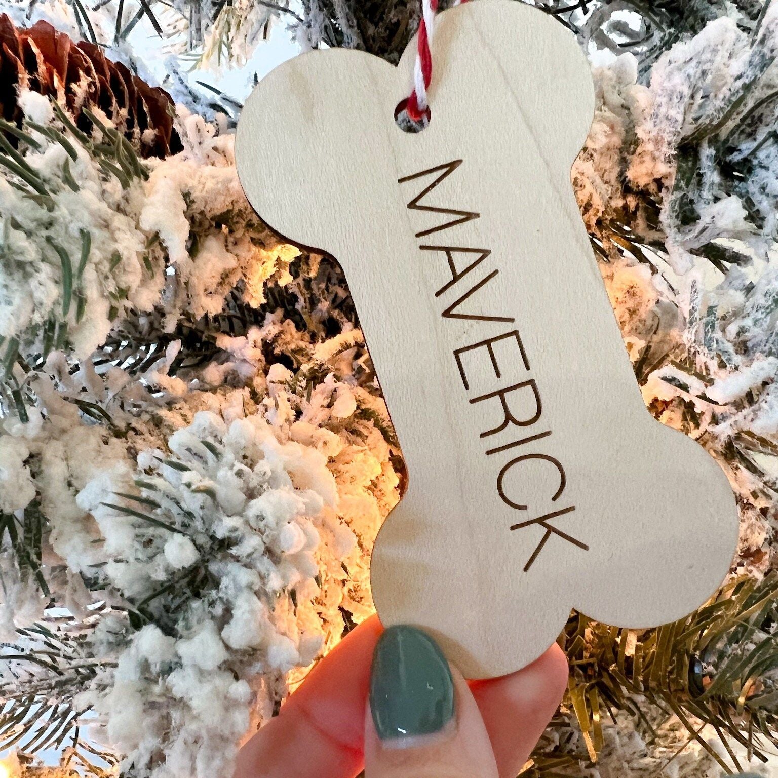 Custom Pet Name Christmas Ornament (Bone shape) being held up against a flocked Christmas tree backdrop.