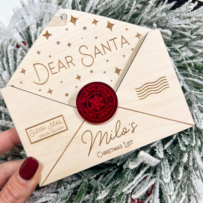 Personalized Wooden Envelope Ornament with "Milo's" engraved, shown hanging on a green Christmas tree branch.