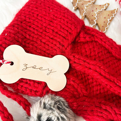Wooden Dog Bone Stocking Tag with "Zoey" engraved, shown hanging from a red stocking with fuzzy trim.