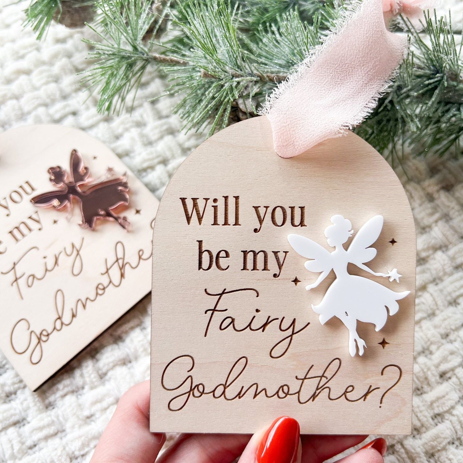Hand holding the Layered Acrylic Fairy Ornament, highlighting its size (3.2 x 3.9 inches) and use as a unique godmother announcement.