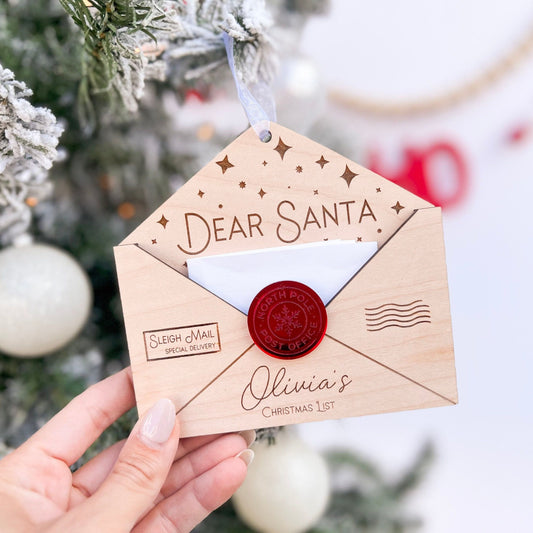 Personalized Wooden Envelope Ornament with "Olivia's" engraved, shown hanging on a green Christmas tree branch.