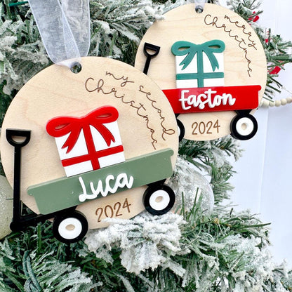 Two Baby's Christmas Ornaments side-by-side, showcasing different custom wagon and bow color options.