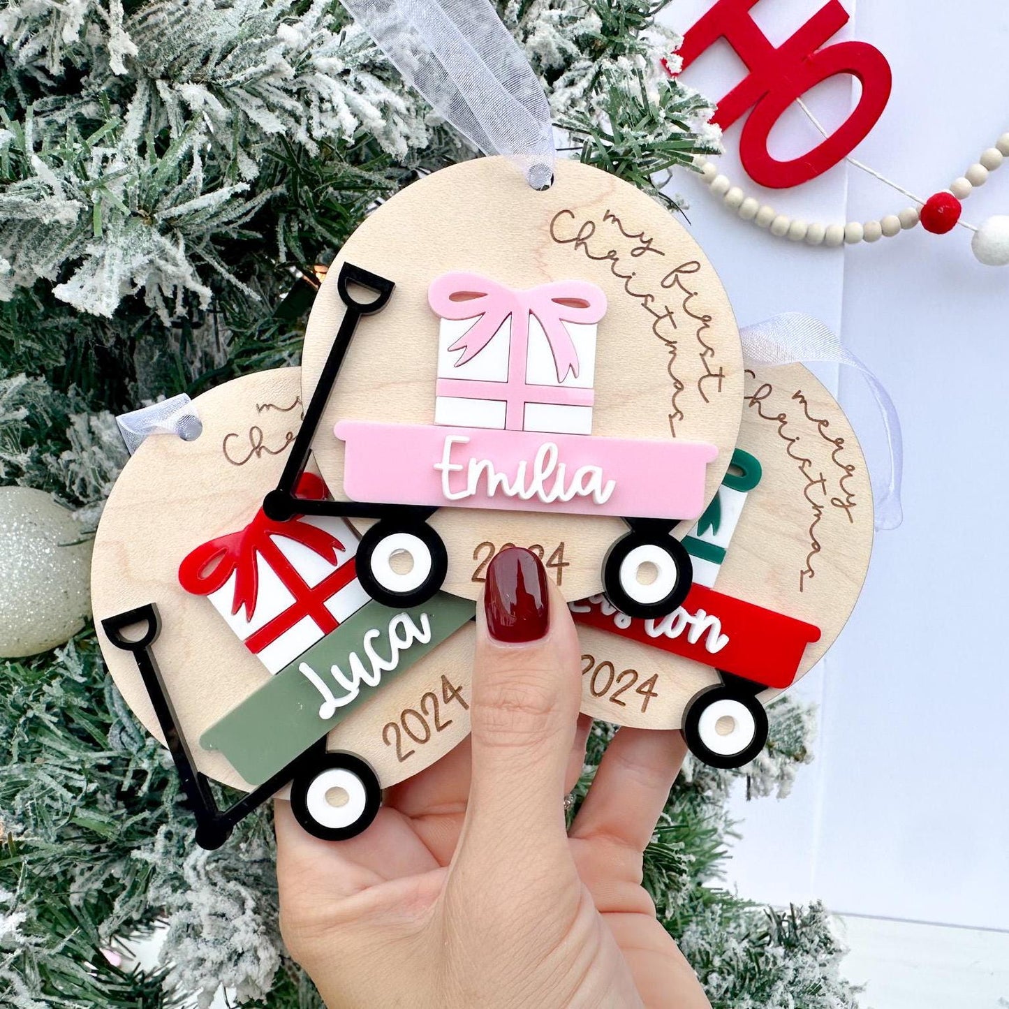 Baby's Christmas Ornaments side-by-side, showcasing different custom wagon and bow color options (e.g., pink wagon with a pink bow) and different sayings.