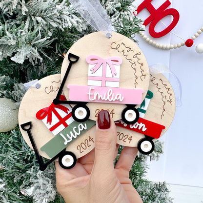 Baby's Christmas Ornaments side-by-side, showcasing different custom wagon and bow color options (e.g., pink wagon with a pink bow) and different sayings.