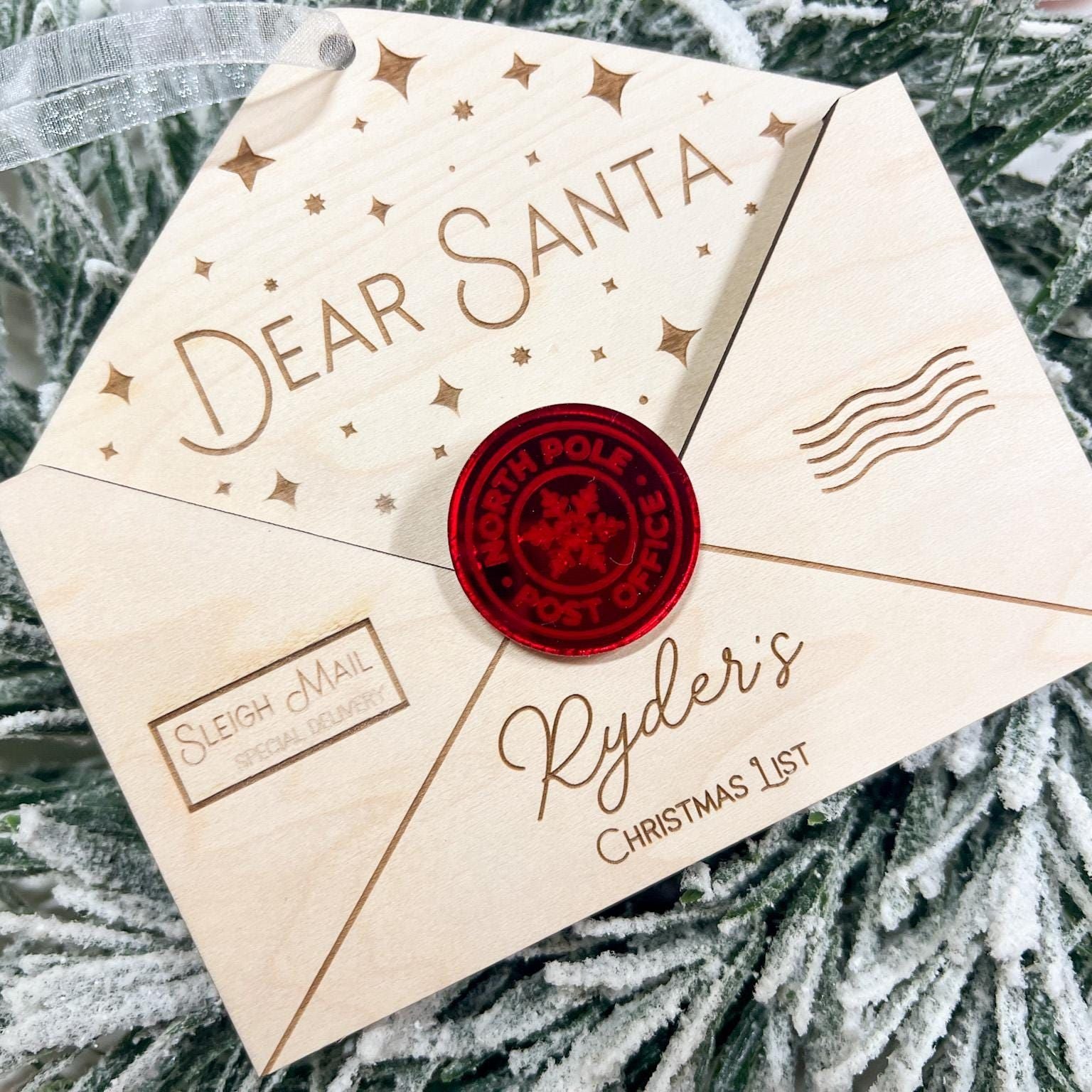Personalized Wooden Envelope Ornament with "Ryder's" engraved, shown hanging on a green Christmas tree branch.