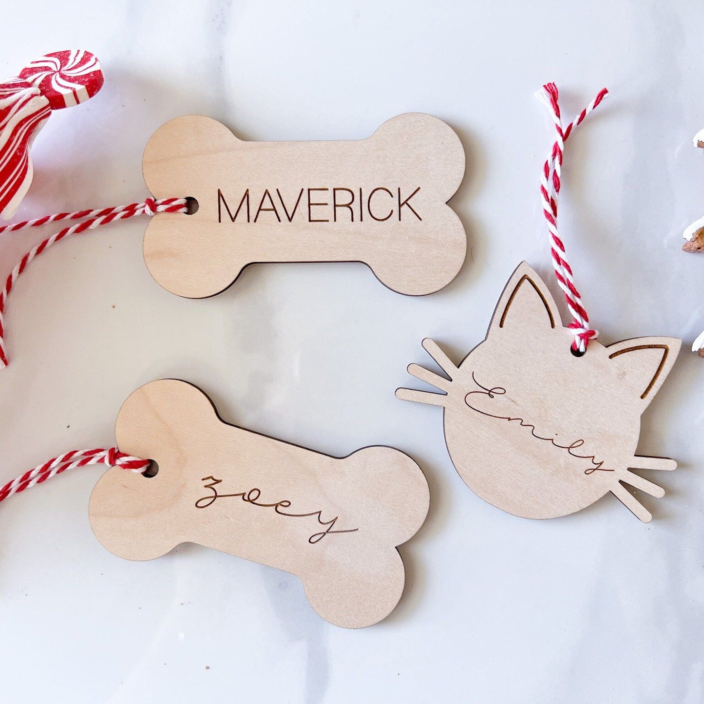 Personalized Pet Stocking Tags on a white surface, showing two Bone tags and one Cat tag with various names and fonts.