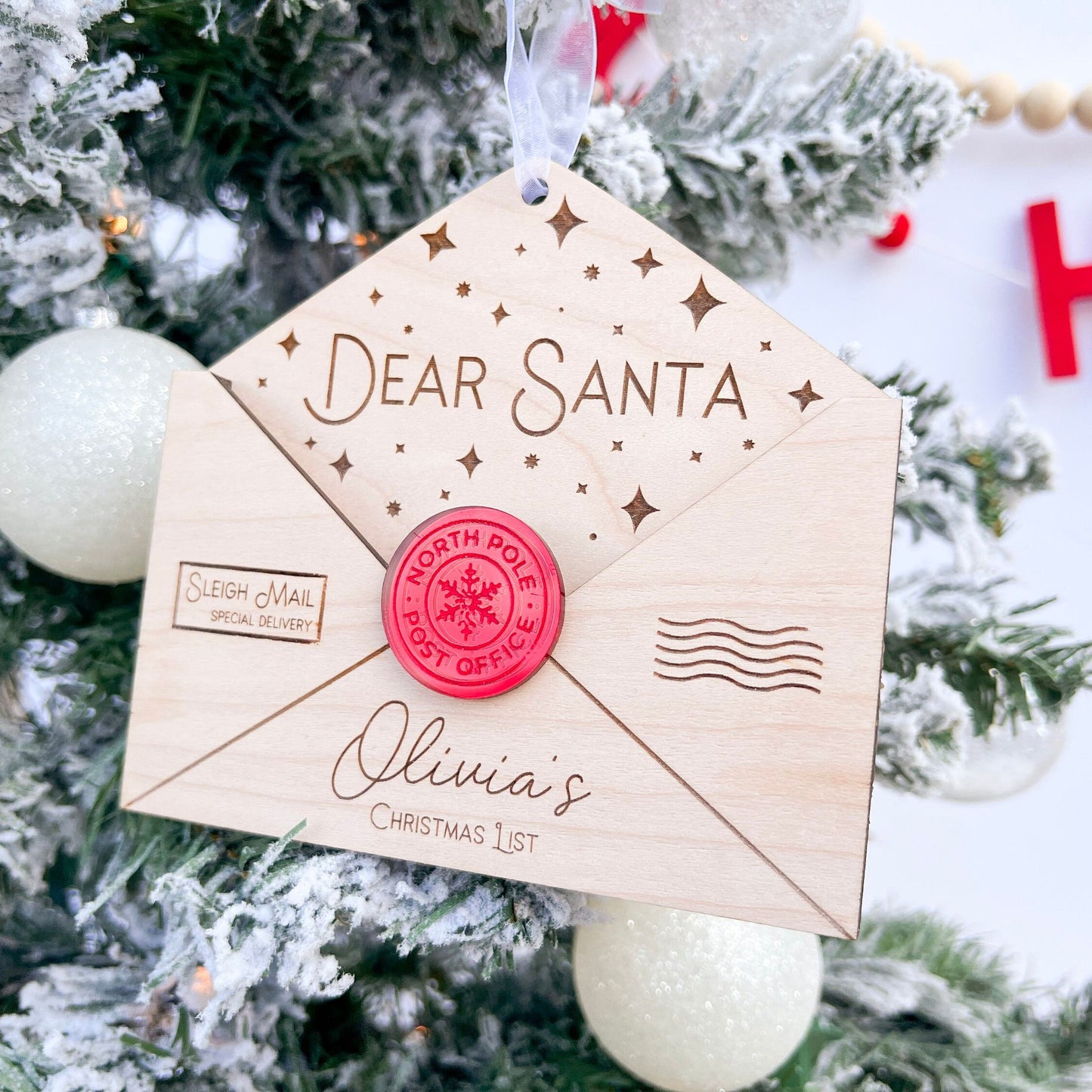 Personalized Wooden Envelope Ornament with "Olivia's" engraved, shown hanging on a green Christmas tree branch.