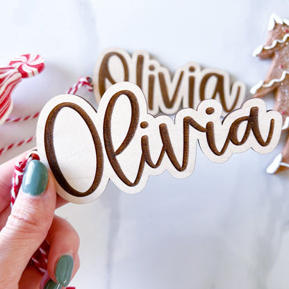 Hand holding a Personalized Wooden Tag in the script font against a wintery Christmas decoration backdrop.