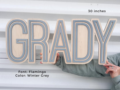 Personalized baby boy nursery sign.  Flamingo font with Winter Grey accents. The sign is 30 inches long. The letters are layered, creating a dimensional effect. The sign is held by a person.