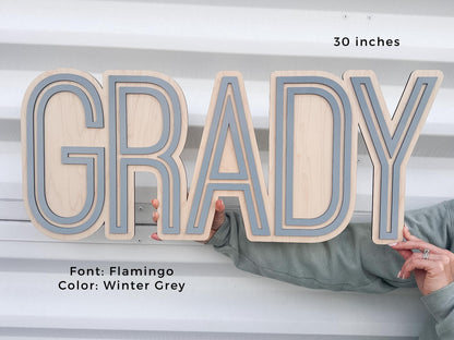 Personalized baby boy nursery sign.  Flamingo font with Winter Grey accents. The sign is 30 inches long. The letters are layered, creating a dimensional effect. The sign is held by a person.