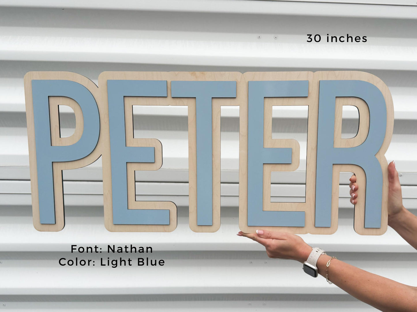 Light blue boy nursery name sign.  Wooden sign spelling "PETER" in light blue letters, 30 inches wide. The font is Nathan. The letters are layered on a natural wood background. The sign is held by a person.