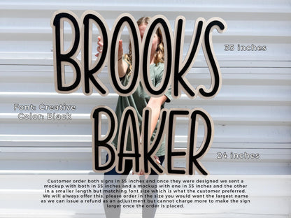 Black personalized nursery name sign.  Wooden sign spelling "BROOKS BAKER" in a creative font with black lettering. The top sign is 35 inches long, and the bottom sign is 24 inches long. The sign is held in front of a white background.