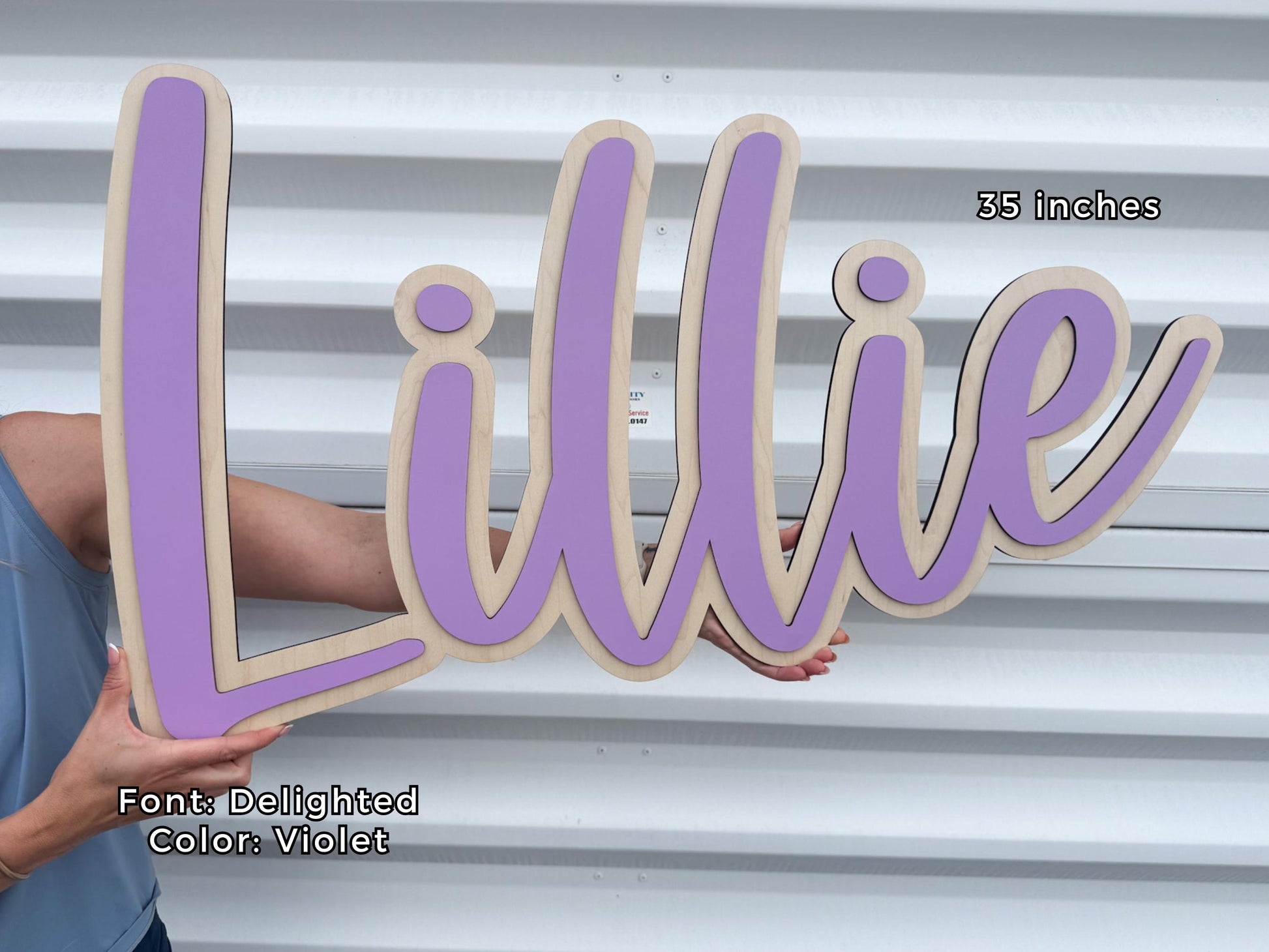 A wooden nursery name sign spelling "Lillie" in a cursive font, with a violet color and a natural wood border. The sign is 35 inches long. The font is "Delighted" and the color is violet.