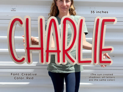 Personalized nursery Wooden sign spelling "CHARLIE" in red and natural wood. The sign is 35 inches long and features a creative font. The text "Font: Creative Color: Red" is also visible.