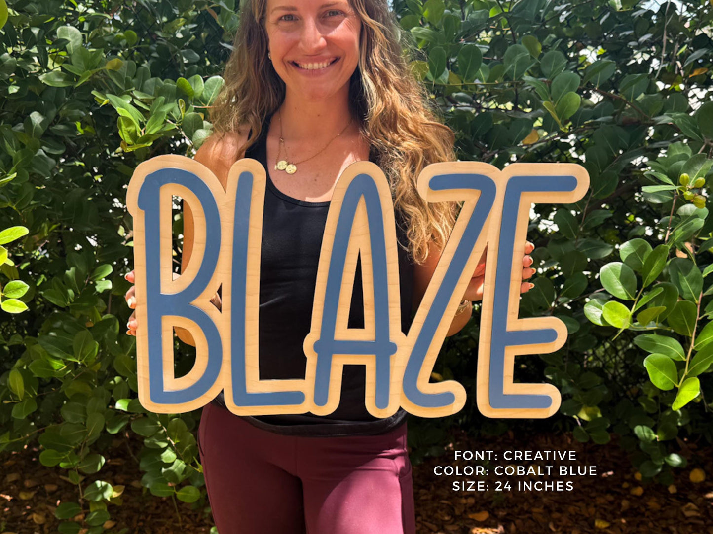 Cobalt Blue personalized nursery sign.  A wooden sign with the word "BLAZE" in a creative font, outlined in cobalt blue. The sign is 24 inches in size. The background features lush green foliage.