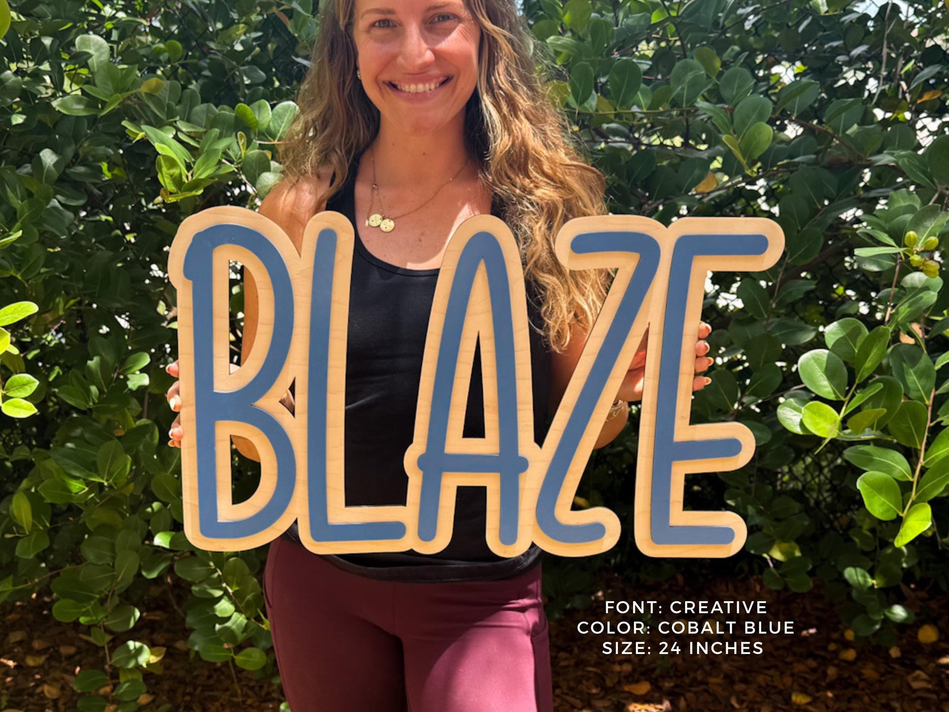 Cobalt Blue personalized nursery sign.  A wooden sign with the word "BLAZE" in a creative font, outlined in cobalt blue. The sign is 24 inches in size. The background features lush green foliage.